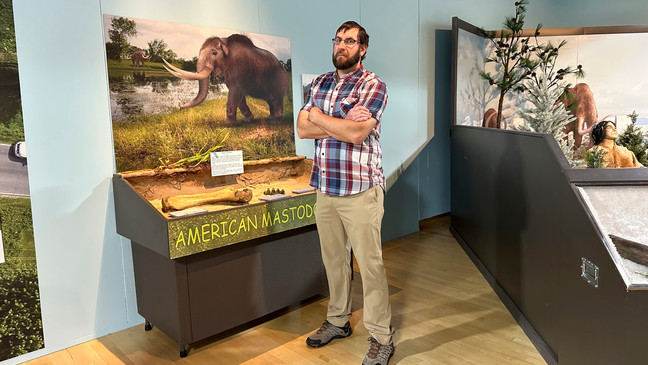 Cory Redman, science curator at the Grand Rapids Public Museum, stands near a mastodon display at the museum on Thursday, May 18, 2023, in Grand Rapids, Mich. (AP Photo/Mike Householder)