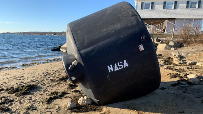 A giant black tank sits on the beach in the Conimicut section of Warwick, Thursday, Dec. 3, 2020. The word "NASA" was apparently painted on it after it came ashore. (WJAR)