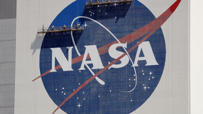 FILE - Workers on scaffolding repaint the NASA logo near the top of the Vehicle Assembly Building at the Kennedy Space Center in Cape Canaveral, Fla., May 20, 2020.  (AP Photo/John Raoux, File)