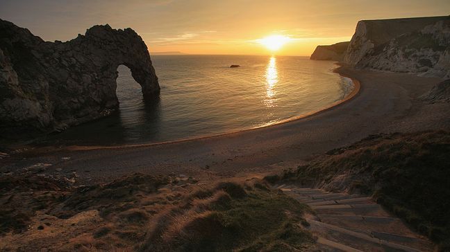 DURDLE DOOR, ENGLAND - MARCH 15:  The sun sets over the sea near Durdle Door on March 15, 2011 in Dorset, England. The natural limestone arch near Lulworth in Dorset, is one of the highlights of the Jurassic Coast, a World Heritage Site.  (Photo by Matt Cardy/Getty Images)