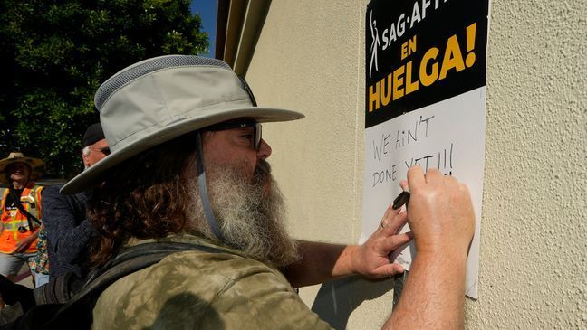 Actor Jack Black writes a sign reading: "We Ain't Done Yet!" as join demonstrators outside the Paramount Pictures Studio in Los Angeles, Tuesday, Sept. 26, 2023. (AP Photo/Damian Dovarganes)