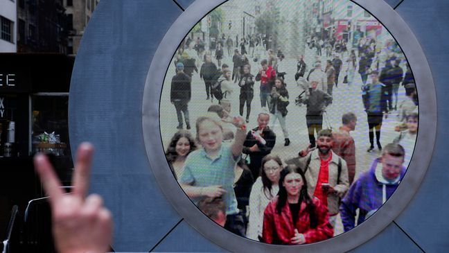 People in both New York and Dublin, Ireland, wave and signal at each other while looking at a livestream view of one another as part of an art installation on the street in New York, Tuesday, May 14, 2024. (AP Photo/Seth Wenig)