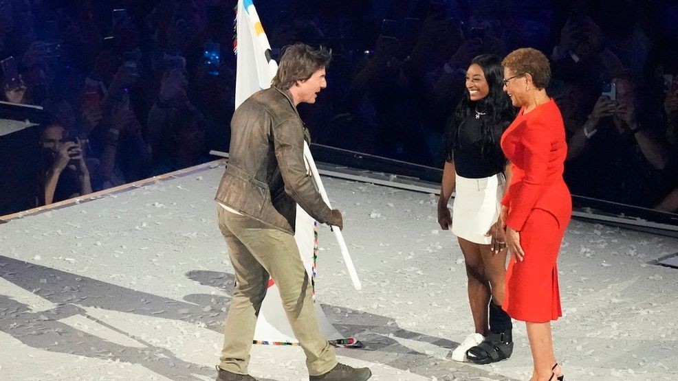 Tom Cruise takes the Olympic flag from Los Angeles Mayor Karen Bass, right, as Simone Biles watches during the 2024 Summer Olympics closing ceremony at the Stade de France, Sunday, Aug. 11, 2024, in Saint-Denis, France. (AP Photo/Rebecca Blackwell)