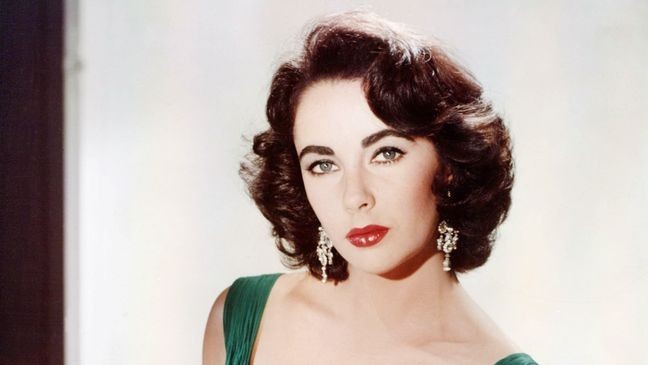 Elizabeth Taylor (1932-2011), British actress, wearing a green sleeveless low-cut dress, with a white fur wrap on the arm of the armchair in which she sits, circa 1950. (Photo by Silver Screen Collection/Getty Images)