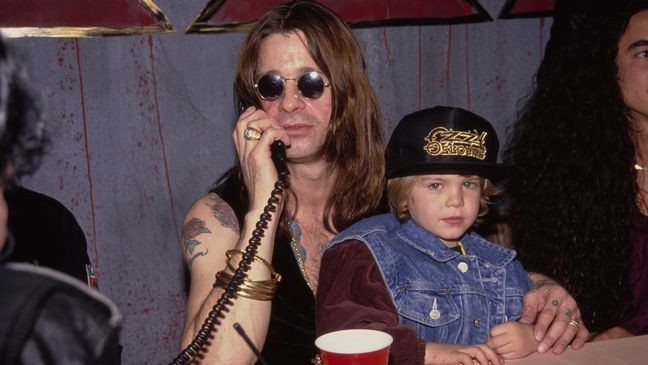 British singer and songwriter Ozzy Osbourne, speaking on the telephone and his son, British television personality Jack Osbourne, wearing an Ozzy Osbourne baseball cap, as Ozzy attends an in-store appearance at the Music Plus record store in Los Angeles, California, 18th November 1991. (Photo by Vinnie Zuffante/Getty Images)