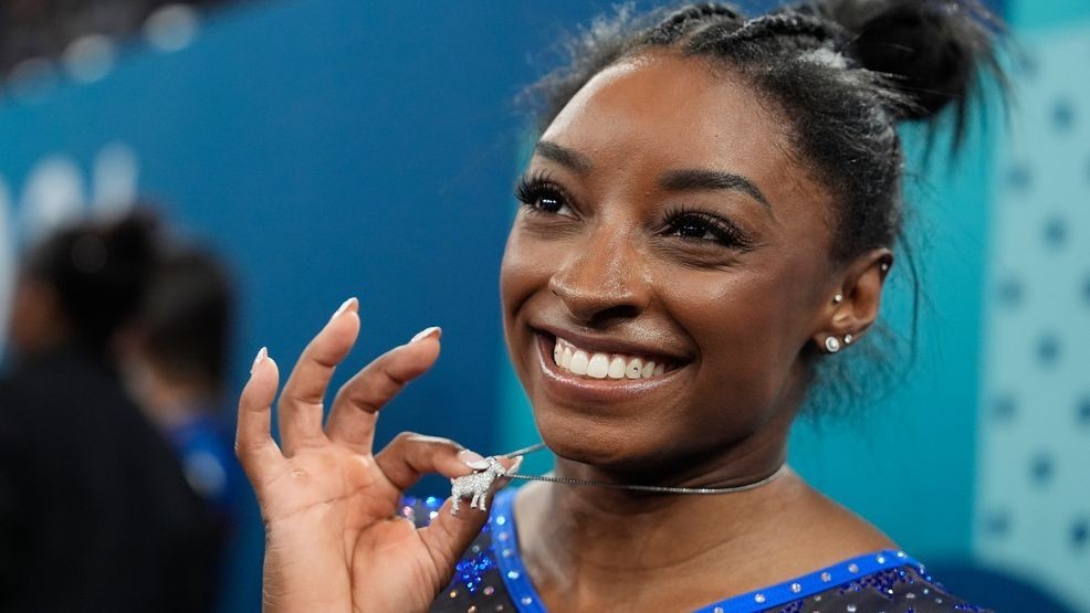 Simone Biles, of the United States, celebrates with her GOAT necklace after winning the gold medal during the women's artistic gymnastics all-around finals in Bercy Arena at the 2024 Summer Olympics, Thursday, Aug. 1, 2024, in Paris, France. (AP Photo/Charlie Riedel)