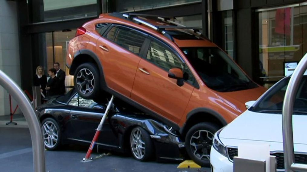 In this image made from video, a Porsche Carrera car is underneath another car in Sydney, Australia Thursday, May 31, 2018. Australian media say a valet drove the soft-top Porsche Carrera under another vehicle Thursday outside the Hyatt Regency Hotel in Sydney. (Australian Broadcasting Corp. via AP)