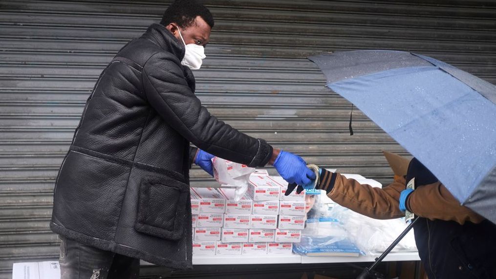 Alex Poam, left, sells gloves to a customer on a street corner in Manhattan, New York, Sunday, April 26, 2020. (AP Photo/Seth Wenig)