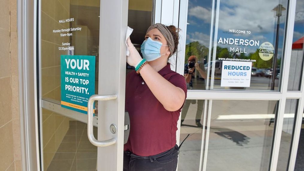 Kendall Ballew an employee of the Anderson Mall cleans the doors before the mall opened to limited business on Friday, April 24, 2020 in Anderson, S.C.  (AP Photo/Richard Shiro)