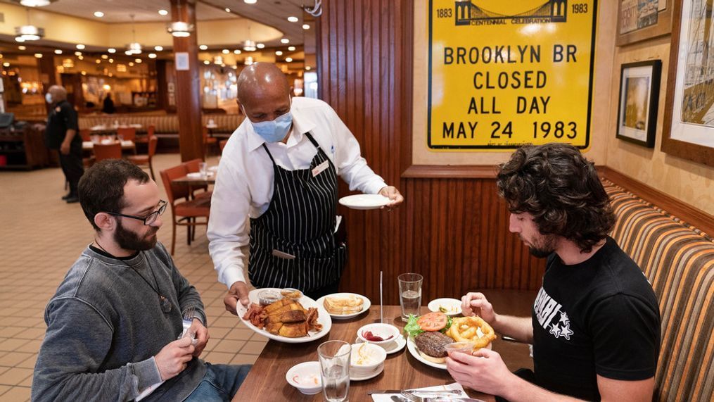 FILE - In this Sept. 30, 2020, file photo, Waiter Lenworth Thompson serves lunch to David Zennario, left, and Alex Ecklin at Junior's Restaurant in New York. New York City will soon require proof of COVID-19 vaccinations for anyone who wants to dine indoors at a restaurant, see a performance or go to the gym, Mayor Bill de Blasio announced Tuesday, Aug. 3, making it the first big city in the U.S. to impose such restrictions.(AP Photo/Mark Lennihan, File)