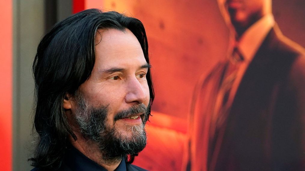 Keanu Reeves, the star of "John Wick: Chapter 4," wears a blue ribbon on his lapel in tribute to his late fellow cast member Lance Reddick, seen in a poster in the background, at the premiere of the film, Monday, March 20, 2023, at the TCL Chinese Theatre in Los Angeles. (AP Photo/Chris Pizzello)