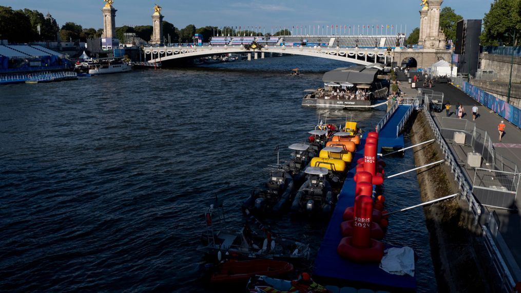 Watercraft and buoys sit along the Seine river as the triathlon event venue on the Pont Alexandre III bridge stands in the background at the 2024 Summer Olympics, Sunday, July 28, 2024, in Paris. (AP Photo/David Goldman)