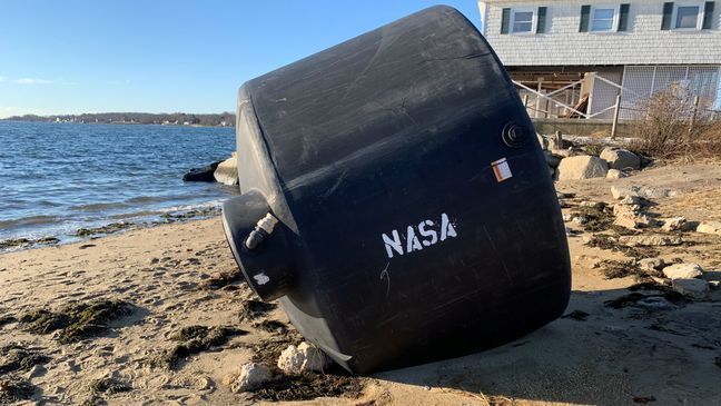 A giant black tank sits on the beach in the Conimicut section of Warwick, Thursday, Dec. 3, 2020. The word "NASA" was apparently painted on it after it came ashore. (WJAR)