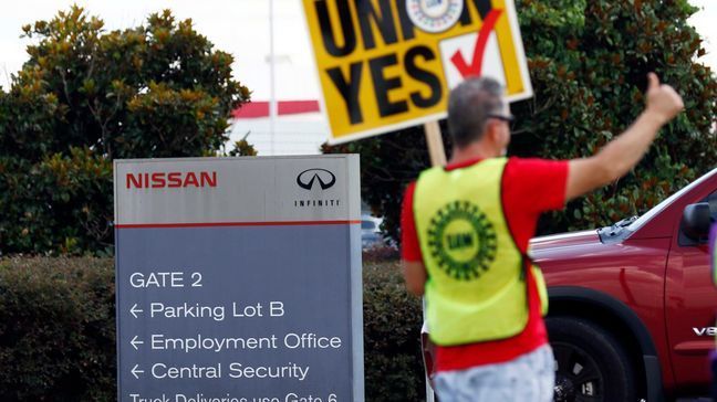 A United Auto Workers sign-bearing member stands outside an employee vehicle entrance at the Nissan vehicle assembly plant in Canton, Miss., and greets each arriving vehicle, Thursday, Aug. 3, 2017. Union members set up informational lines outside employee entrances at the plant and greeted all shifts of workers arriving and leaving, reminding workers to vote for the union. The vote for union representation of line workers runs Aug. 3-4. (AP Photo/Rogelio V. Solis)